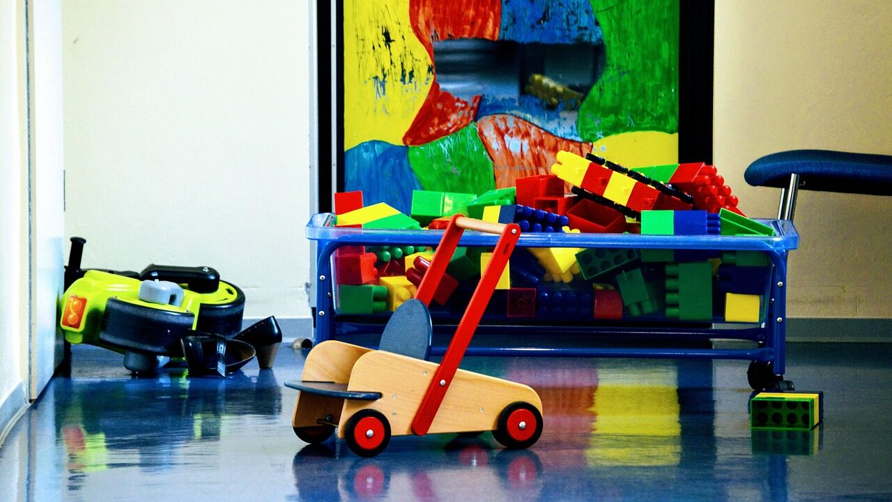 Speelhoek met grote bouwblokken, een houten loopwagen en speelgoedvoertuigen in een ingerichte woning voor kinderopvang